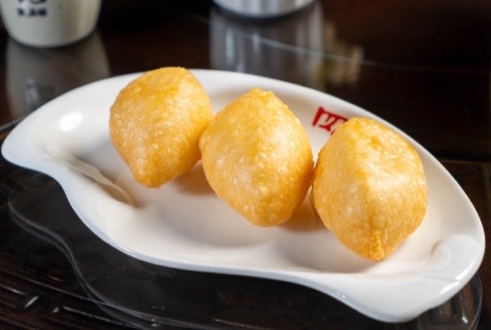 Three golden puffed pastries on a curved white dish
