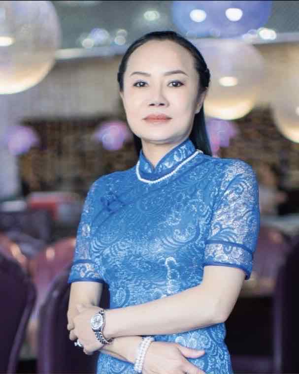 Sijie, founder of Yu by Sijie, in a blue lace cheongsam standing in a restaurant dining room