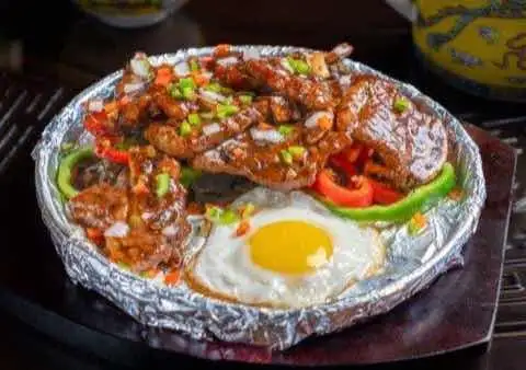 Sizzling beef with peppers and a fried egg on a foil-lined plate